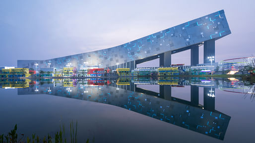 The illuminated façade of the indoor ski slope reflects across the central lake at dusk. © Arch Exist