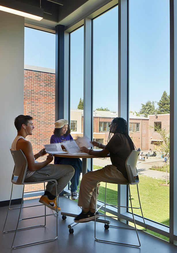 Students gather to socialize and study with a view of the campus from floor to ceiling windows, providing ample daylight.