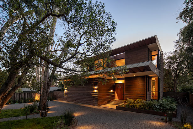 Photography by Taiyo Watanabe. At the front of the home, one is greeted by the California live oak and Eucalyptus trees that define the local landscape and keep in proportion with the generous home, while the airplane hangar style garage door, finished with charred siding, “disappears” when closed.