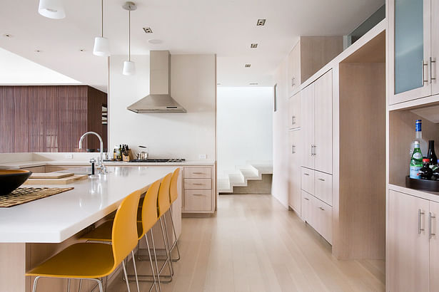 The cabinets are white oak, the counter Caesarstone, and the cantilevered concrete stairs of the entry are visible in the background.