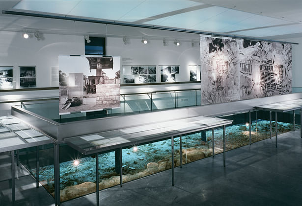 An aerial photo of Gusen concentration camp taken in 1944 hanging over the excavated area connects the finds to the site and acts as a room divider blocking the view of the pictures showing the liberation of the camp presented at the end of the exhibition.