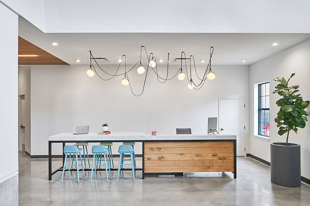 A custom-made steel-framed table replaced the previous bunker-like reception desk. The new version doubles as a co-working space for employees. Image Credit: Keith Isaacs