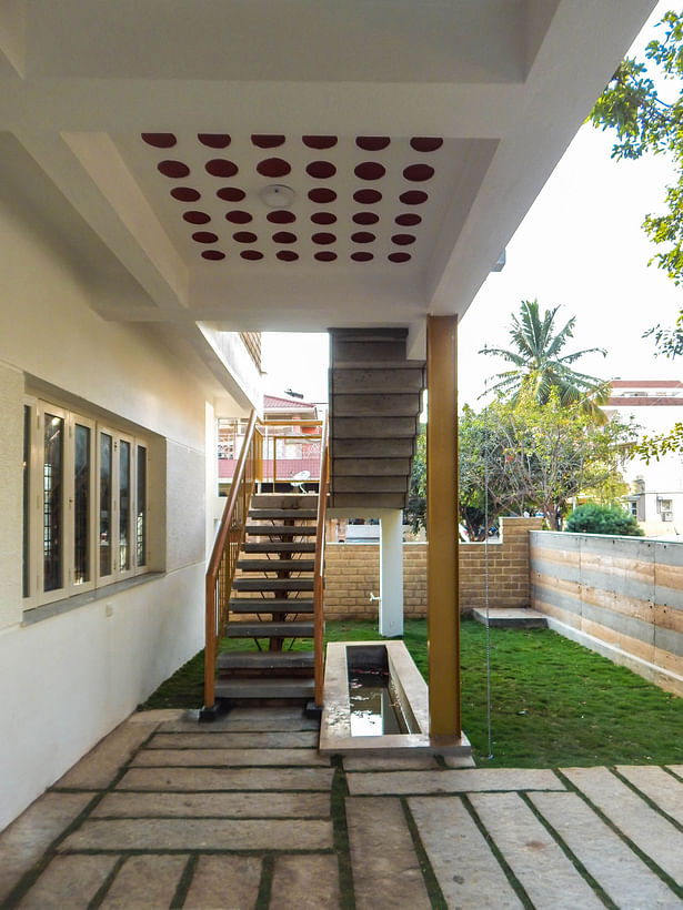 The combination of unfinished sadarhalli stone steps and exposed concrete folded plate staircase along with a Lilly pond welcomes one at the entrance leading to the upper floor