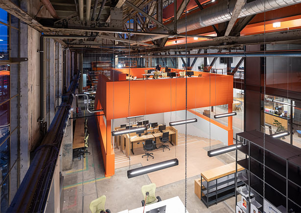 A lowered working pit, where oil was once collected, has been transformed into an orange furniture element. This element includes a mezzanine level with places for concentrated work and a view to the outside.