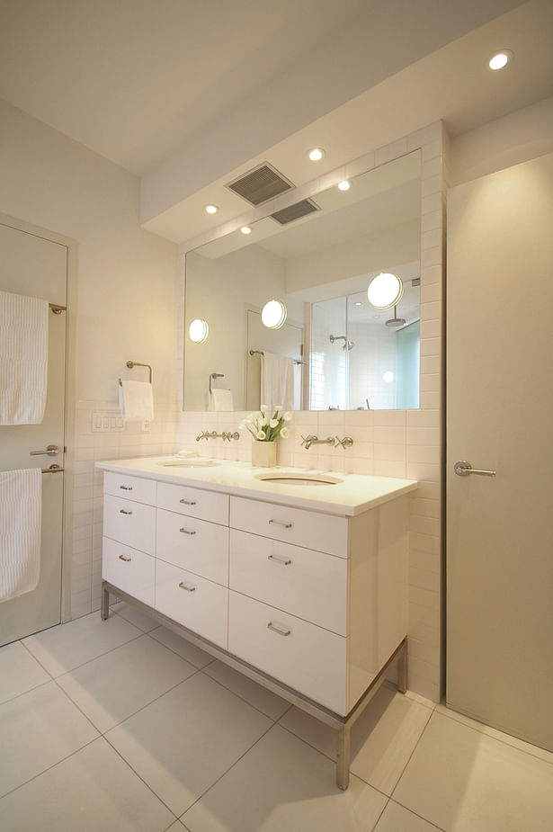 The large double vanity features wall-mounted fittings and a large mirror set flush with the surrounding tile border; large 'can' lights were recessed into the wet wall beyond the mirror to provide brilliant illumination while keeping the perimeter of the room crisp and taught. The vanity cabinet features custom stainless steel legs reminiscent of details used elsewhere in the apartment.