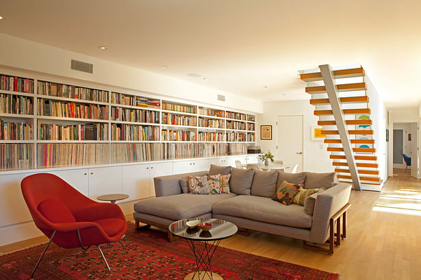The lower floor has been turned into a den, where formerly it had been more divided up. A long bookcase of vinyl records and books frames the room.