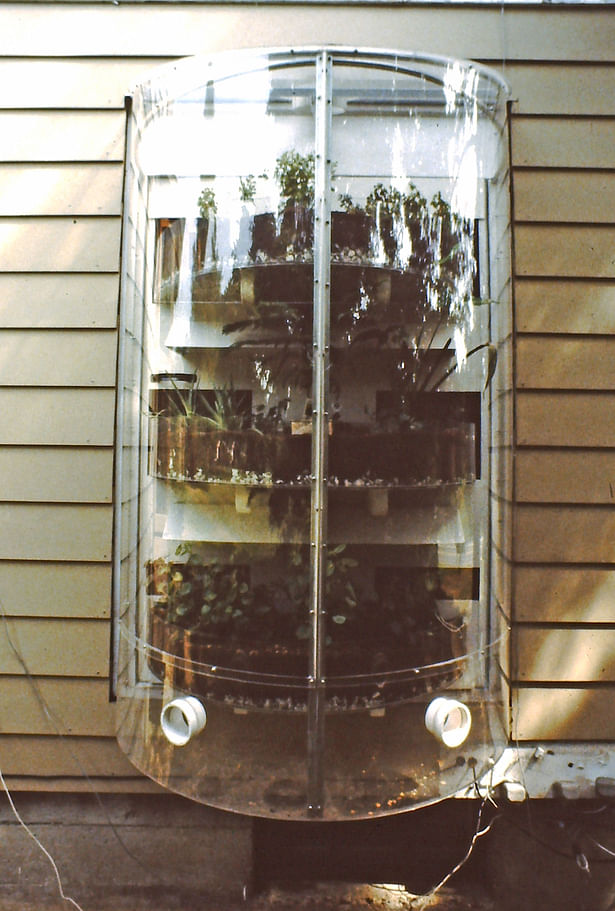 The Solar Round, 1980. A small greenhouse module hung onto a house with built-in solar thermal mass and plant shelves. during the day the plants are on the outside of the house contained within the plastic cylinder. At night the plants and solar thermal mass rotate to the inside.