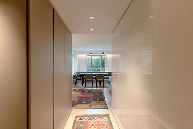 The existing entry was very dark. Recessed lights were added. Complementing the custom metallic-colored millwork, a wall of glossy white panels bounces light, making the space feel brighter, and hides two 'hidden' doors to a coat closet and a small office closet.