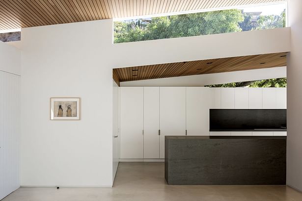 'Clerestory windows mark overhanging sections of the roof while emphasizing its butterfly shape. The dining area flows into a new kitchen, which features new lacquered cabinetry and an inset area for the cooktop. A door to the left provides access to the carport.'