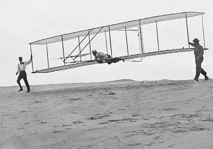 Photo of the Wright brothers' third test glider being launched at Kill Devil Hills, North Carolina, on October 10, 1902. Wilbur Wright is at the controls, Orville Wright is at left, and Dan Tate (a local resident and friend of the Wright brothers) is at right