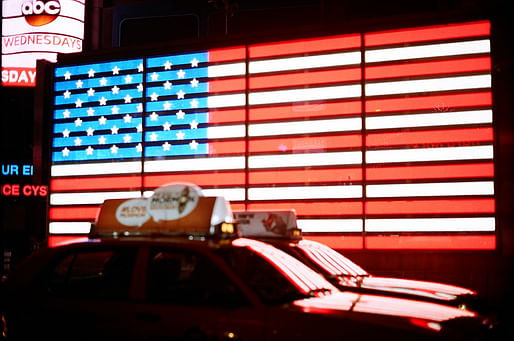 Taxis drive past an illuminated American flag in New York Times Square. Photo: Harold Navarro/Flickr.