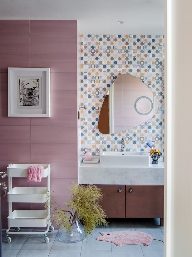 The bathroom of the daughter's is very decorative, with a mosaic wall of rich tiles, a modern mirror shaped as a drop of water, and a small pink ornament.