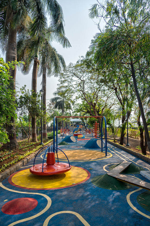 A bright and colourful children's play area shaded by lush green trees.