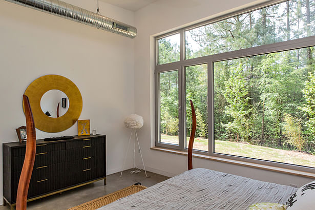 An oversized window frames a view of the nearby forest in the master bedroom.