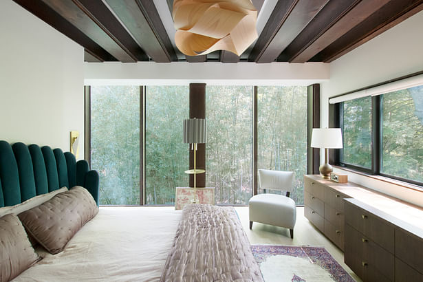The primary bedroom includes restored wood beams, a built-in custom dresser, and a view to the bamboo thicket.