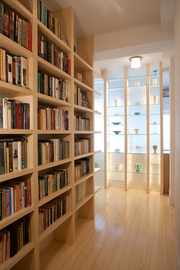 New bookshelves and a translucent shelf wall lead visitors to the main living space while obscuring direct views into the kitchen. The cubistic etched glass shelf wall is backlit by daylight, or it can glow from within by way of cleverly concealed accent lights built into the vertical supports.