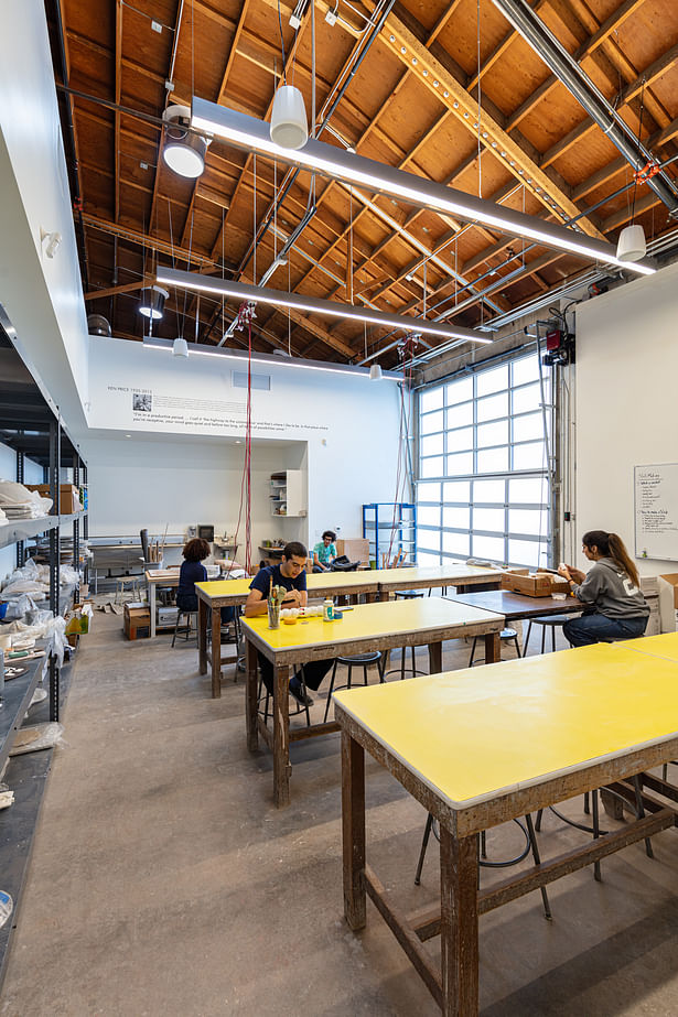 The ceramics studio, which simultaneously functions as an enclosed classroom and enables the experience of the grandeur of the volume of the warehouse. Natural daylight pours in through a glass roll-up door, through which is accessed an outdoor kiln.