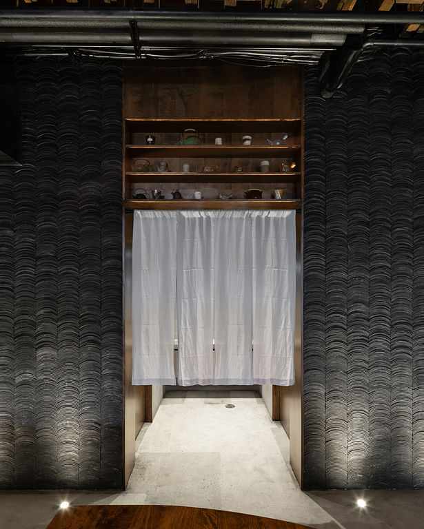 The tiled wall is gently interrupted by a wooden frame, displaying over-head decor and housing the unisex bathroom installations.
