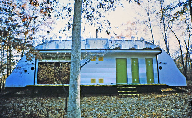 North side of the house with built-in firewood storage, main entry, and dry food storage access doors.