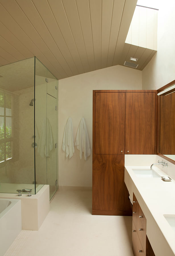 The master bathroom integrates stone, wood, and light with its Douglas fir vaulted ceiling, a freestanding walnut cabinet, a limestone counter and floor, and custom skylights. 