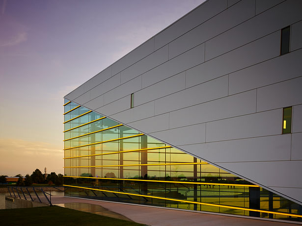 The sculptural building prow incorporates symbolic lines as if ripples in the water. A surprising overlap of two gold window “notes” make the interior volume known.