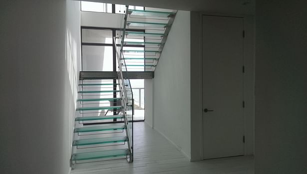 Dual stringer staircase with a frosted glass landing & treads, tempered glass railings, and a stainless steel handrail.
