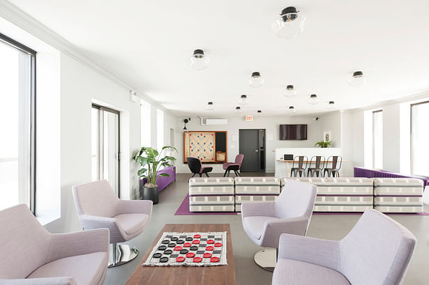Lounge chairs form a casual meeting space around a large coffee table. At the opposite end, another gaming area is formed around an oversized Scrabble board. The existing radiators, one functioning and one not, where both painted bright purple calling attention to the side walls and views to the lake and the city. 