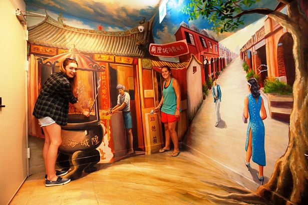 Two girls taking photos with 3D wall painting, which depicts a traditional Taiwanese temple and old street in Taipei.