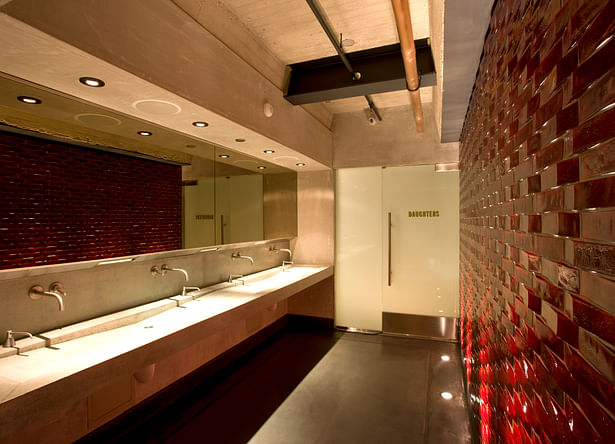 The architects at (fer) studio designed a community washroom which acts as a focal space for separate restrooms, with bock beer colored mosaic tiles, a bronze mirror and concrete sink.