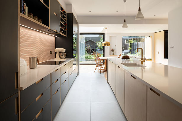 The kitchen is placed at the heart of the home. Door and drawer fronts are Formica and birch plywood by Plykea, with the carcasses from Ikea. Worktops are Silestone, and splashback tiles from Claybrook, both lit from above by an LED strip recessed into the wall units. Photograph by Adam Scott