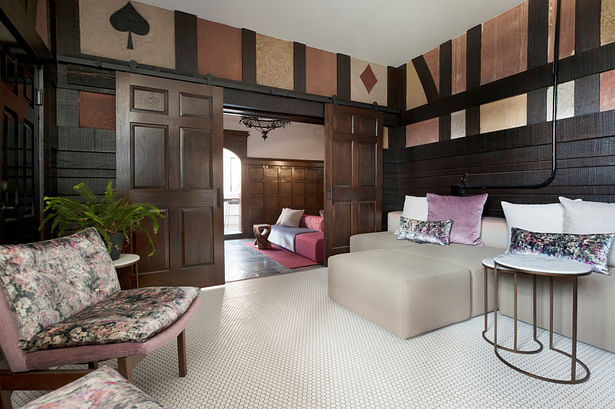 A former storage room off the lobby was transformed into a conversation lounge. The original doors leading to the lobby were re-purposed as sliding doors to accommodate a raised floor level connecting this area with a residential corridor. Half-timbered walls with suits of playing cards were restored and inspired the tones in the velvet accents. Another large sectional from Stylex lines one full wall and is covered in an embroidered Xorel fabric for durability against spills in this secluded...
