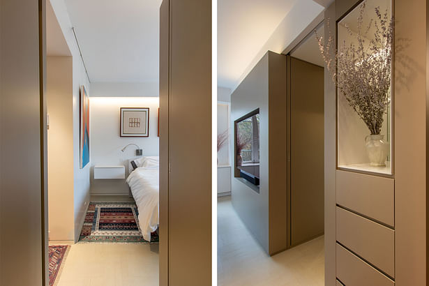 The backside of the appliance garage volume houses a TV niche facing the master bed. A hall connecting to the bathrooms is lined with more metallic-colored millwork, housing a dresser and niche.