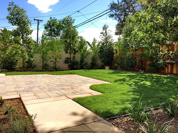 A modest backyard with patio and lawn.