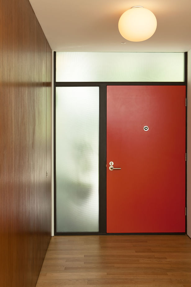 A view of the entry from inside. A mid-century palette and simple modern graphic of warm walnut, textured glass, painted door, and stained wood door jambs.