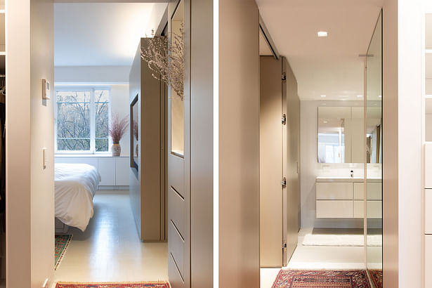 A primary bath and a powder room are located off the hallway running behind the kitchen. Custom doors were created to look like a continuation of millwork panels when closed. Continuing the notion of hardware-less cabinets, flush recessed pulls were used, so there's no hardware projecting from the bathroom doors.