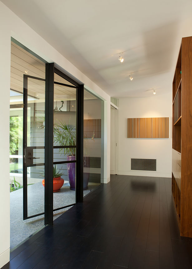 View of the entry area, where the original front wall of the house was opened up with large sheets of glass, and a custom steel/glass door inserted in the middle of the wall. Custom freestanding walnut casework helps define this entry area.