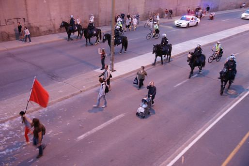 A protester carrying a red flag is followed by policemen on horseback in Montreal in 2012. Credit: Nicholas Korody