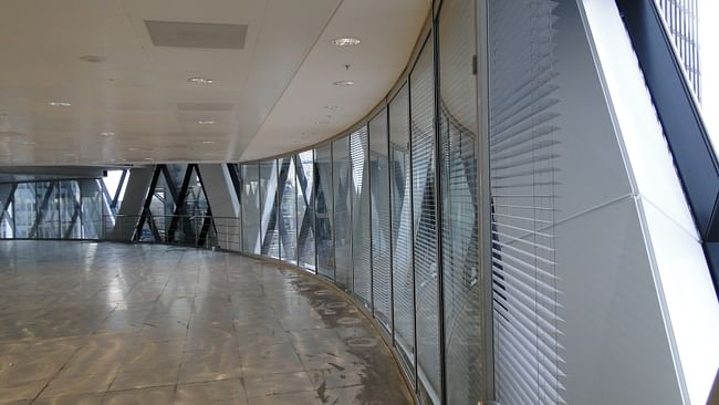Shown here where it opens into the office floor at the base of one of the six-story atriums, the Abluft enclosure sandwiches blinds and encased diagrid struts between the exterior curtain wall and an inner curtain wall of rectangular glass sheets. Photograph by Jonathan Massey.