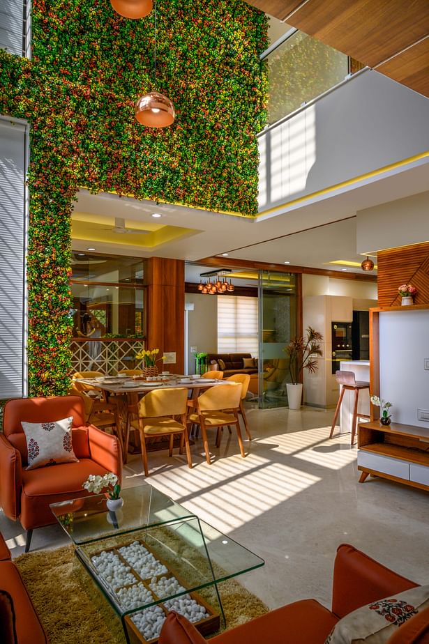 a stunning family sitting with a huge void space above connecting the ground floor to the highest ceiling of the house. With an artificial vertical garden in its backdrop, this space becomes even more appealing and colorful. This volume creates a drama of light and shadows through-out the day across the interiors with the triple height window. 