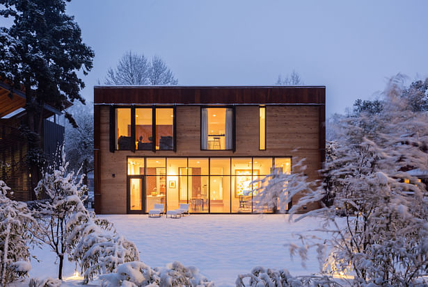 Warm light glows through the modern addition's extensive glazing on a snowy evening.