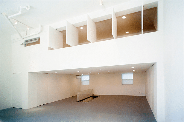 A view of the renovated gallery reconfigured as a large open space with mezzanine living quarters above, with operable wall panels for privacy. It also features an operable skylight opening into the basement living space. 
