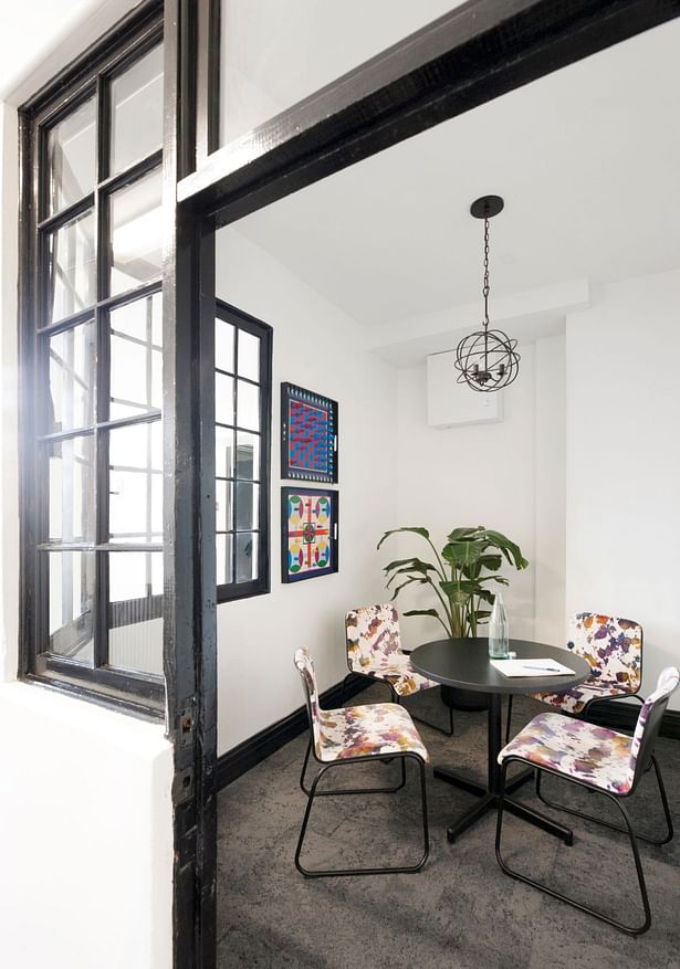 This intimate meeting room was created from another existing storage space. The window frames were painted black in keeping with the steel exterior windows. A modern patterned velvet makes a bold statement against the neutral Interface carpet tiles, while the game boards and new iron fixture hint at elements in the other rooms.