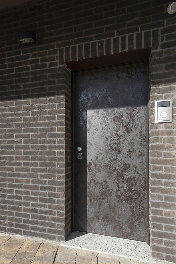 The main entrance door is coated with a “rusty brown” metal to merge wiht the dark brick facade. @Tino Gerbaldo