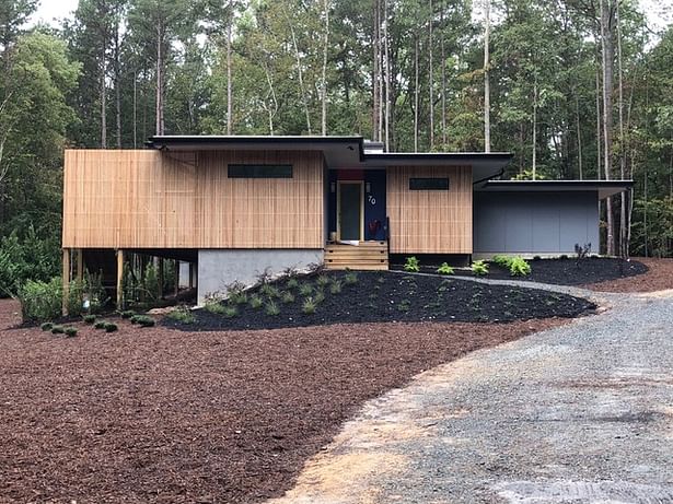 On the front elevation, a 'veil' of cypress slats softens the modern house in the wooded setting. Thin horizontal windows maintain privacy.