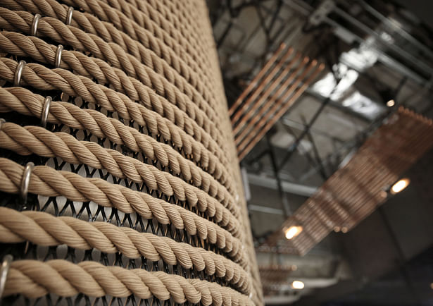 Close-up image of a rope-clad column, and the copper conduits on the ceiling beyond. 