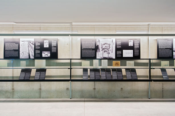 Explanatory texts or quotations in two languages: Individual “sheets” placed in a loose and temporary-looking arrangement on the shelf at the bottom of the construction.