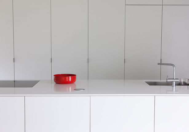 All surfaces in the kitchen are finished in white high-gloss laminate. The unobtrusive metal handles finish the minimalistic ensemble. Photo by Arno de la Chapelle.