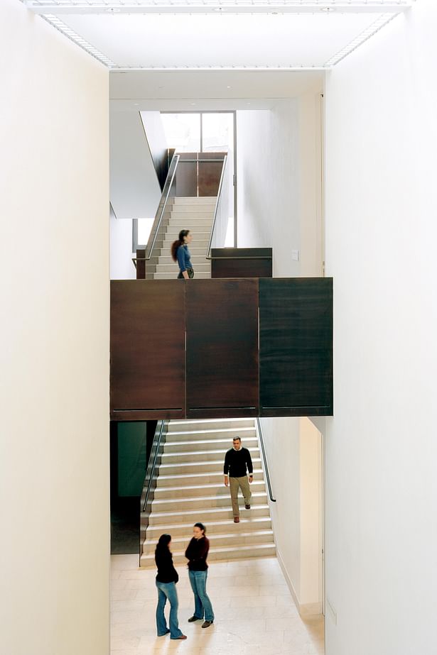 Double-height stair hall, located between permanent collection in the 17th-century palaçio and the changing exhibition wing. Oxidized steel-plate guardrails evoke the dark wood of the historic interiors.