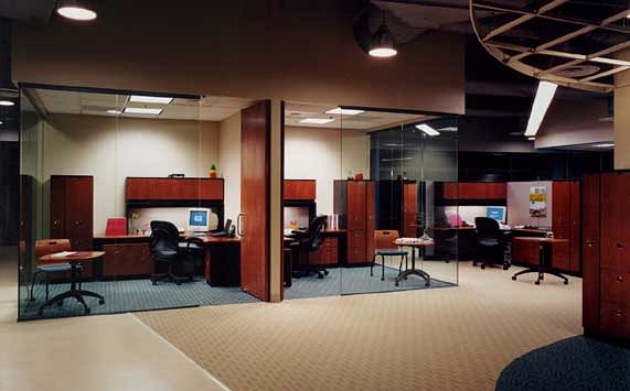 Large open plan office area with systems furniture work stations and glass partitioned offices for senior employees.