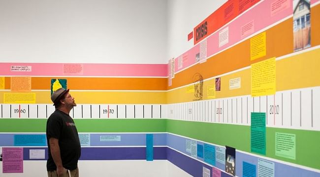 A rainbow-colored timeline of 20th-century American housing on the walls wraps around the exhibit, each strand of the rainbow explaining the different factors leading up to the current state of the U.S. housing industry. Photo by Marianne Williams.